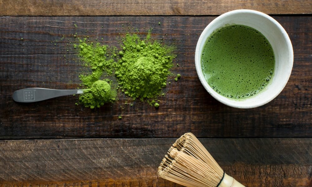 green plant in white ceramic mug beside brown wooden brush, green tea types