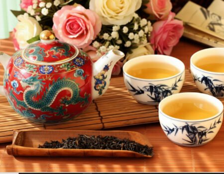 Ornate Chinese teapot with dragon and floral design, accompanied by three cups of tea and fresh roses.