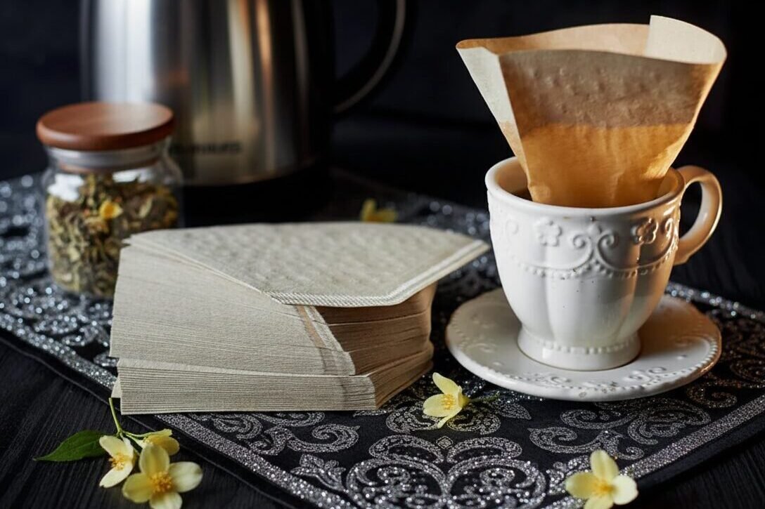 Coffee setup with filters, teacup, kettle, and flowers on a decorative mat in elegant arrangement.