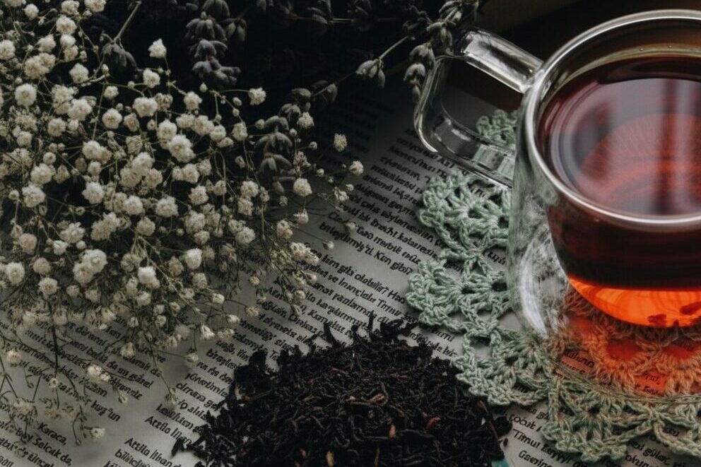 Glass cup of black tea with dried flowers and loose leaf tea on newspaper background.