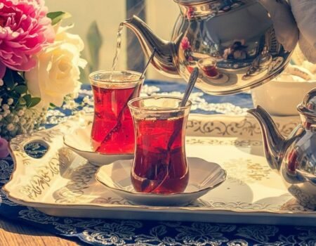 Elegant tea setting with two glasses of red tea and a silver teapot, adorned with fresh flowers on a tray.