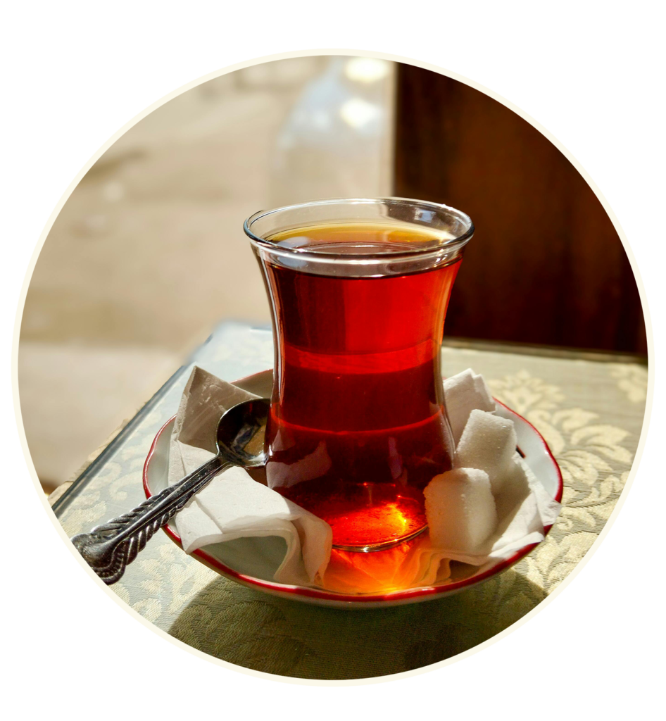 Glass of Turkish tea with sugar cubes and spoon on a saucer, set on a decorative tablecloth, natural light.