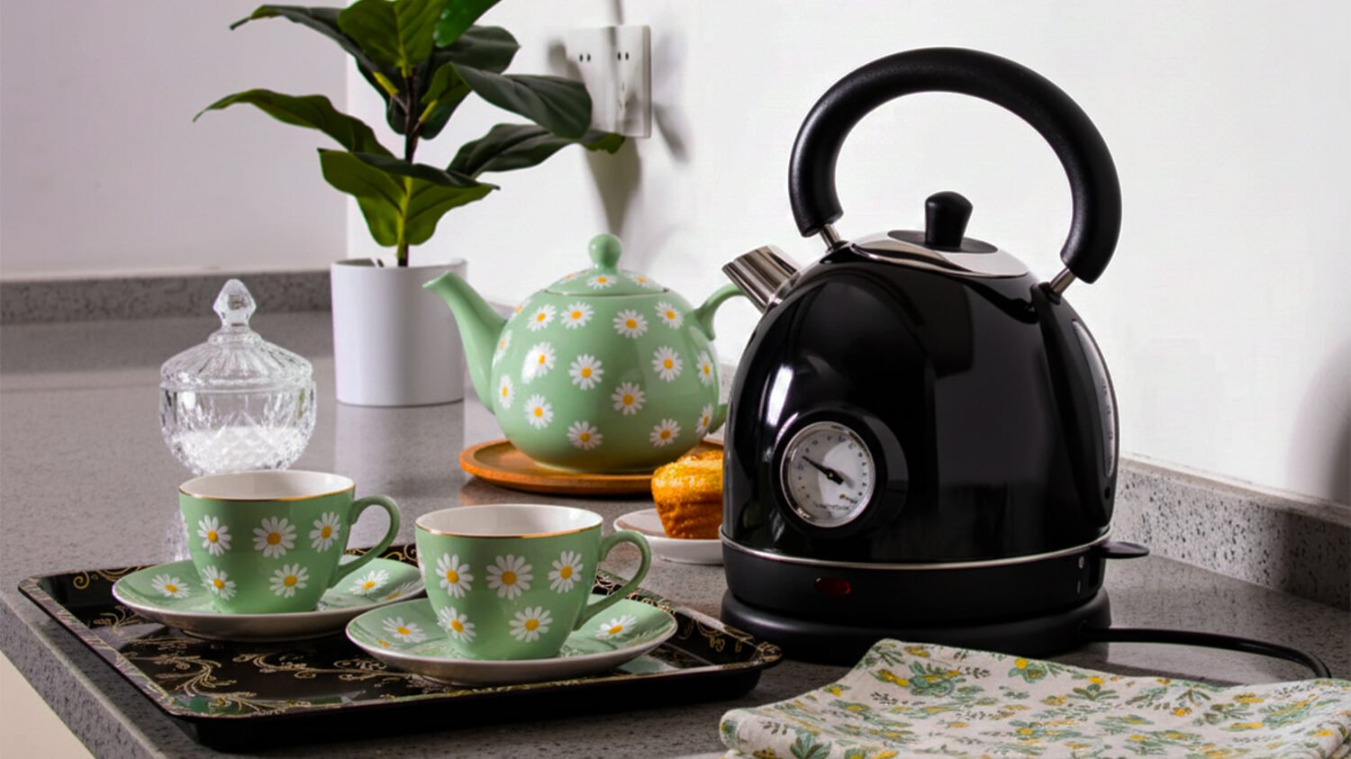 Vintage tea set with floral teapot, cups, and black kettle on a kitchen counter.