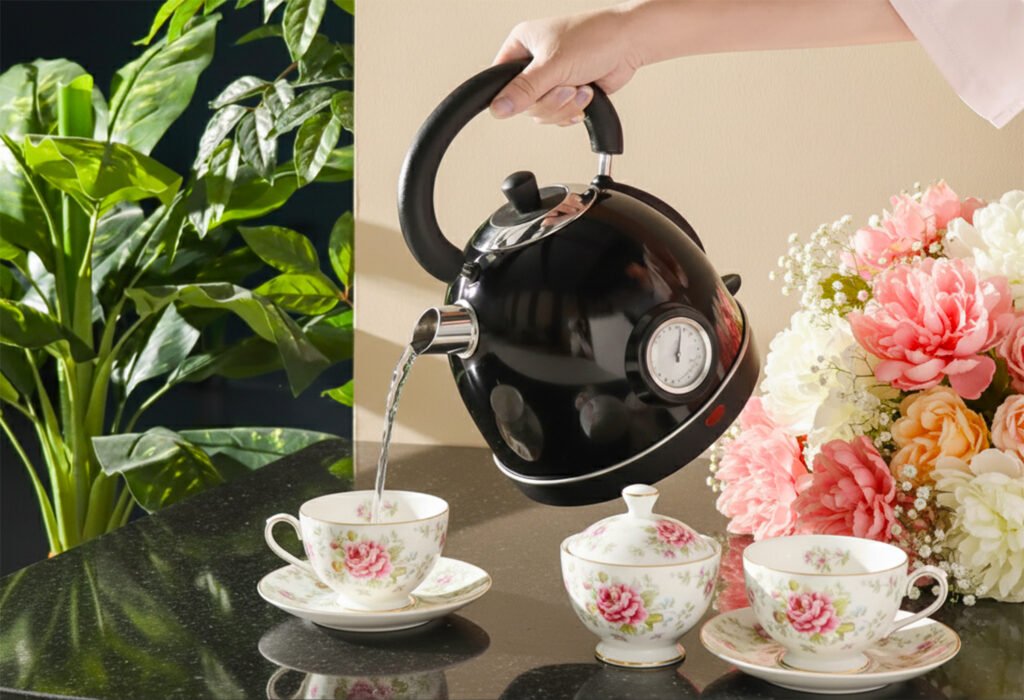 Pouring tea from a black kettle into floral teacups on a countertop, surrounded by flowers and green plants.