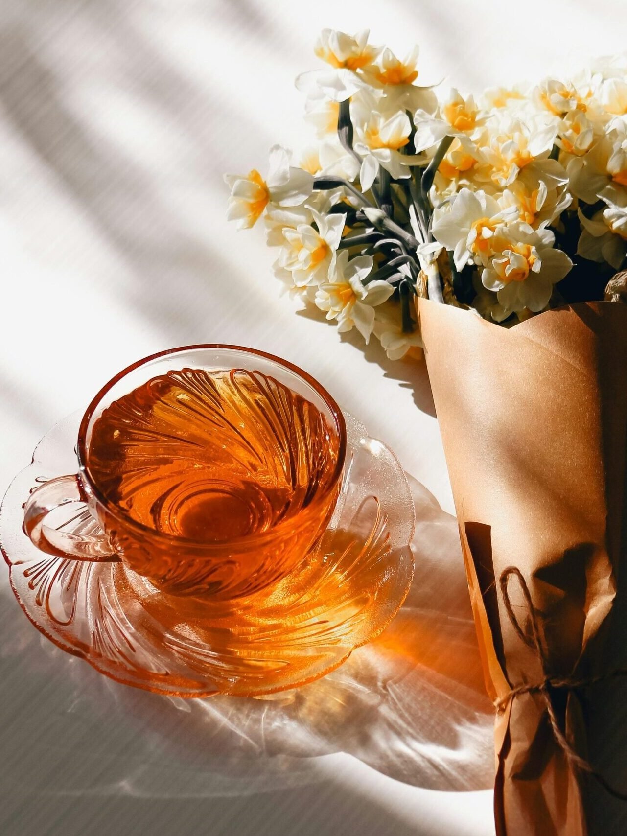 Orange tea in a glass cup with a bouquet of white daffodils on a table.