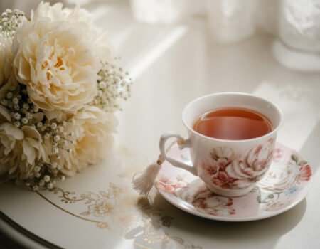 Delicate floral teacup and saucer set with a bouquet on a lace tablecloth, basking in soft sunlight.