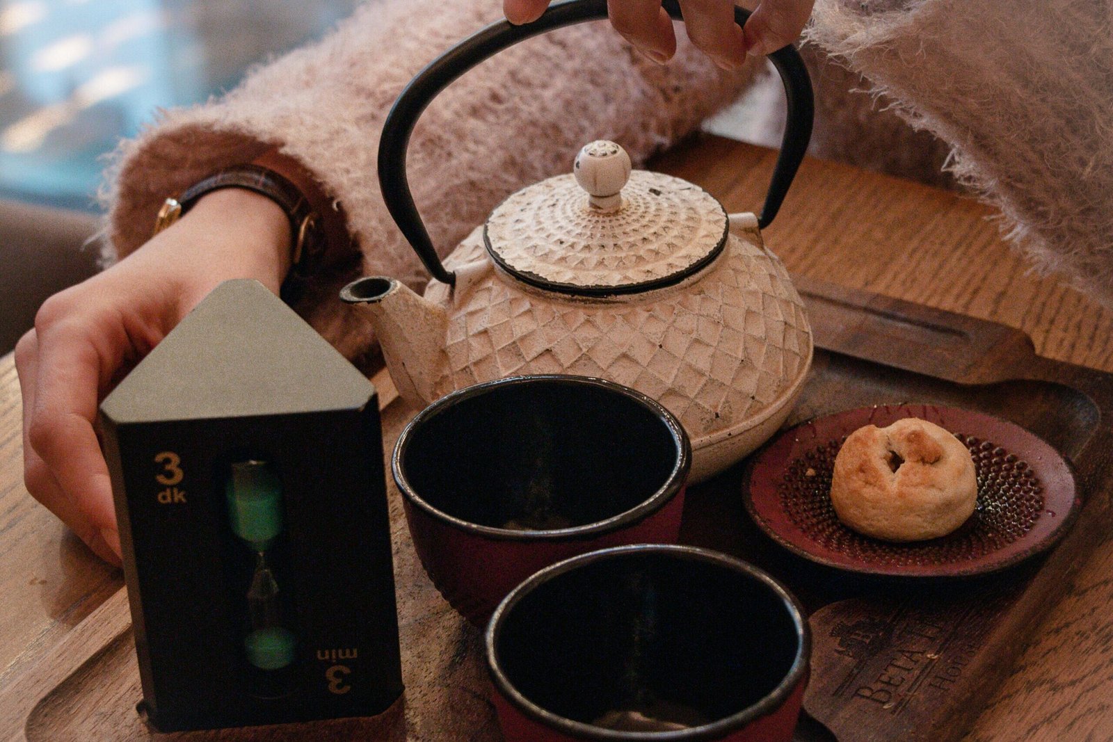 Teapot and cups on a tray with a sand timer and pastry, cozy tea setup on wooden table.