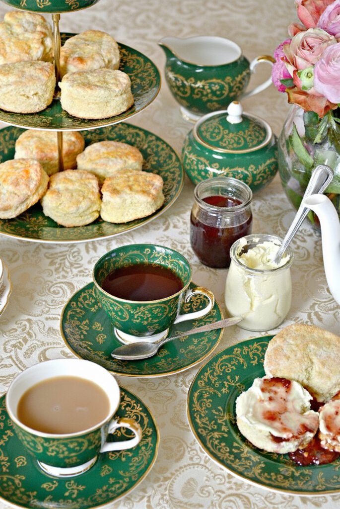Elegant afternoon tea setup with scones, clotted cream, and jam on ornate green china.