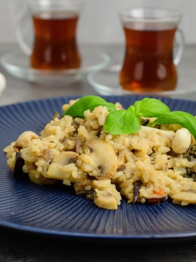 Mushroom risotto garnished with basil on blue plate, paired with tea in glass cups, with fresh basil and mushrooms nearby.