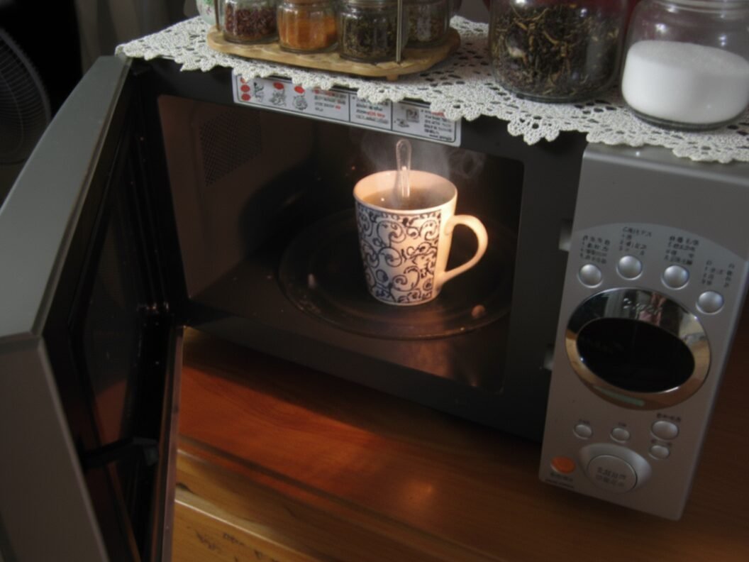Blue ornate mug heating in open microwave on wooden table with spices.