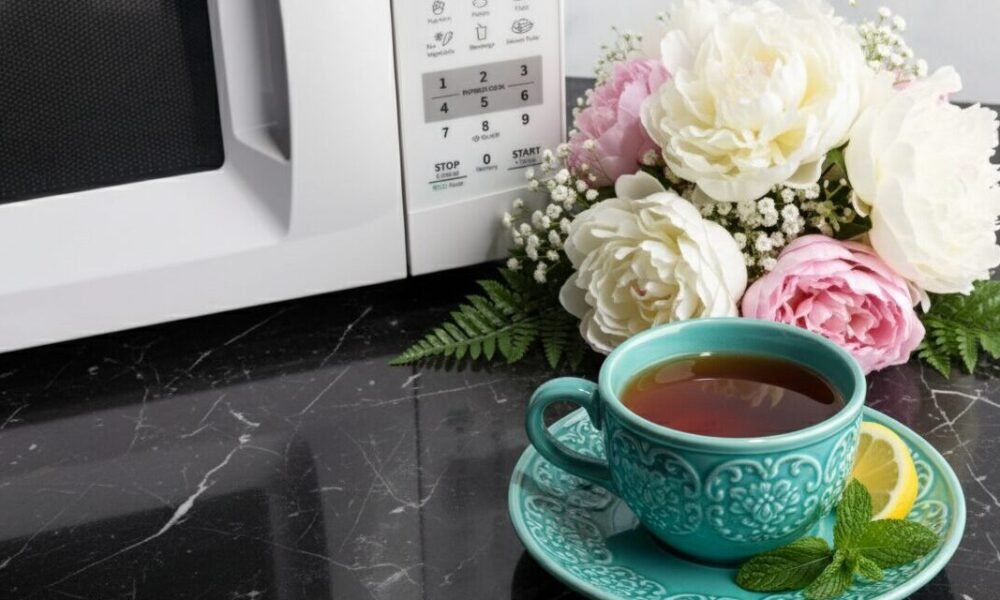 Teal cup of tea with lemon and mint on a marble countertop beside flowers and a microwave.