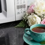 Teal cup of tea with lemon and mint on a marble countertop beside flowers and a microwave.