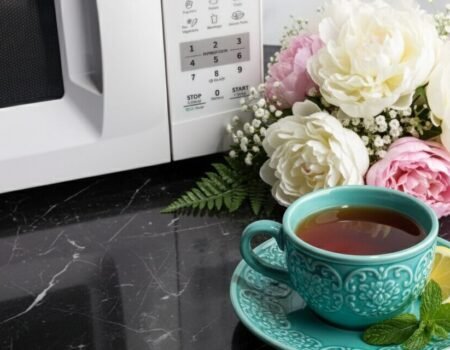 Teal cup of tea with lemon and mint on a marble countertop beside flowers and a microwave.