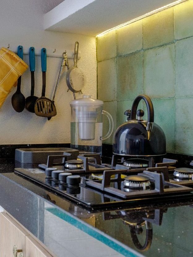 Modern kitchen with gas stove, kettle, and utensils on black countertop; oven mitts and cutlery hanging on the wall.