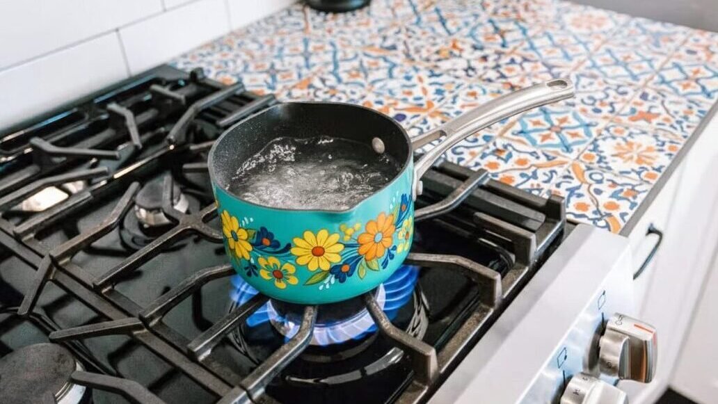 Colorful pot with boiling water on a lit gas stove, with decorative tile backsplash in a cozy kitchen.