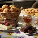 Assorted pastries, tea, and flowers on a table setting, featuring cakes, muffins, and a vibrant floral centerpiece.
