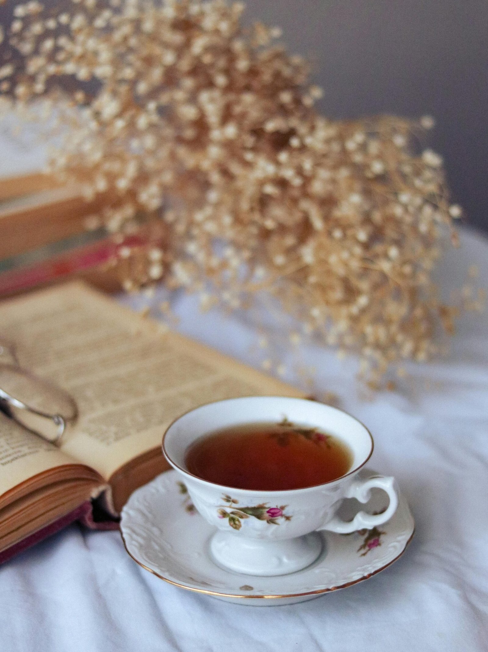 Delicate teacup with tea beside an open book and dried flowers on a table. Cozy and vintage atmosphere.