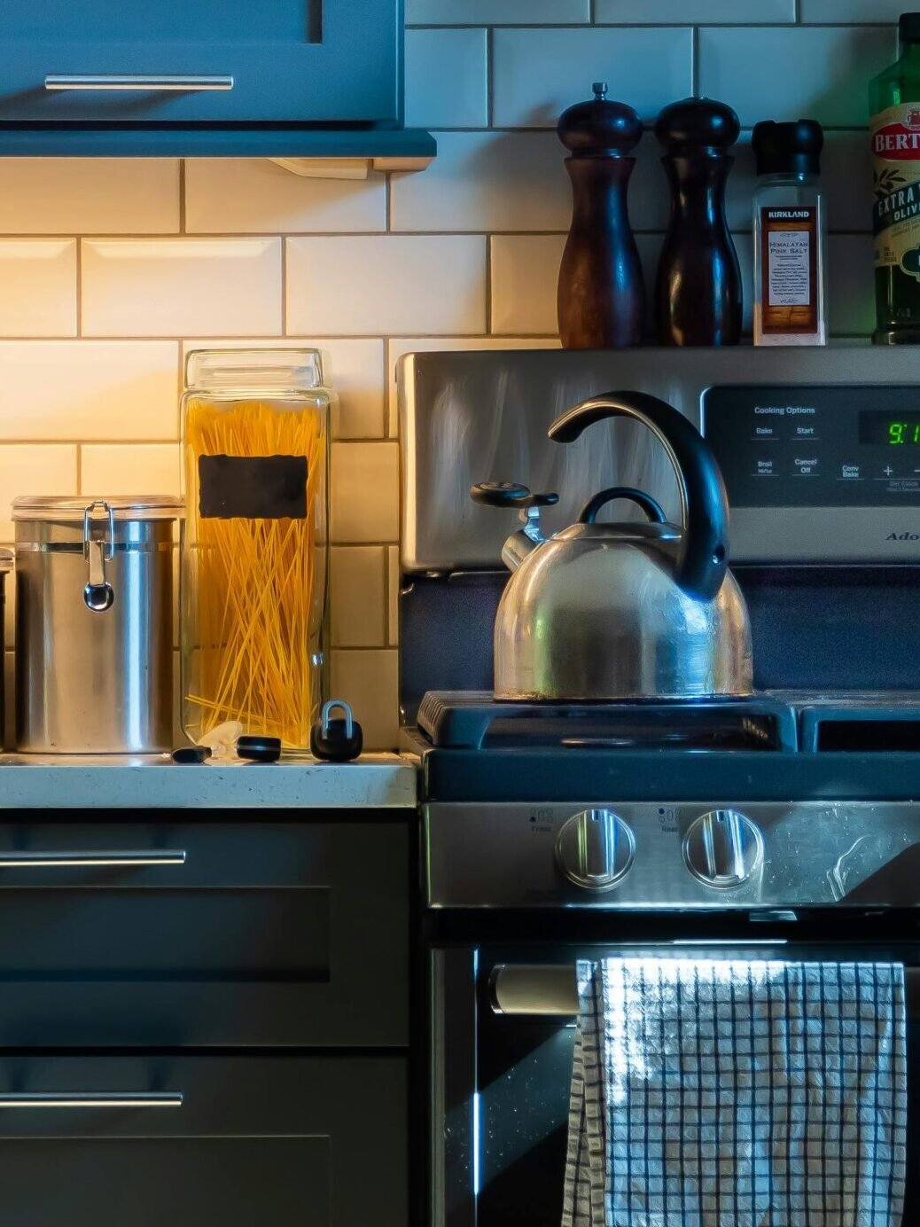 Modern kitchen with subway tile backsplash, teal cabinets, stainless steel appliances, and neatly arranged countertop items.