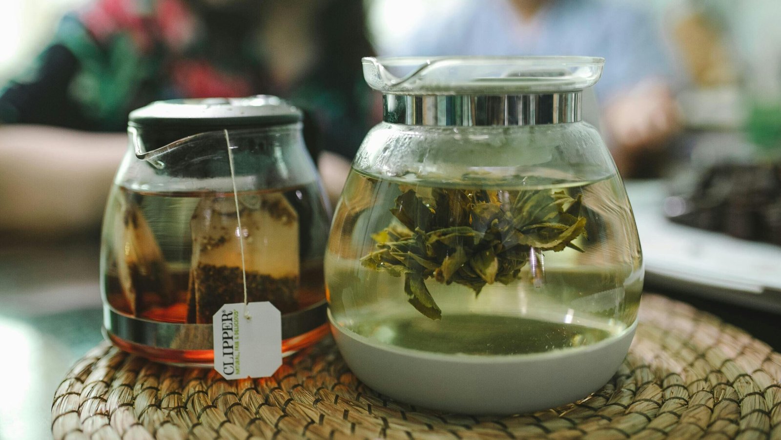 Glass teapots with blooming tea and bagged tea steep on a woven mat, creating a cozy atmosphere.