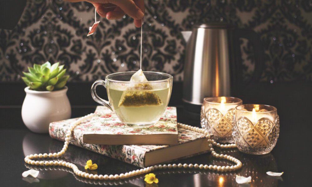 How to Brew Tea Bags: Tips for the Perfect Cup of Tea the Easy Way Hand dipping tea bag into cup, with candles, books, and a succulent on a decorative table setup.