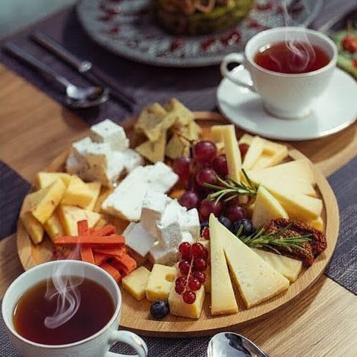 Cheese platter with grapes and tea cups on a dining table.