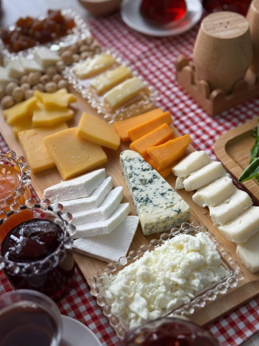 Assorted cheese board with various cheeses, nuts, and jams on a gingham tablecloth for a fresh picnic setup.