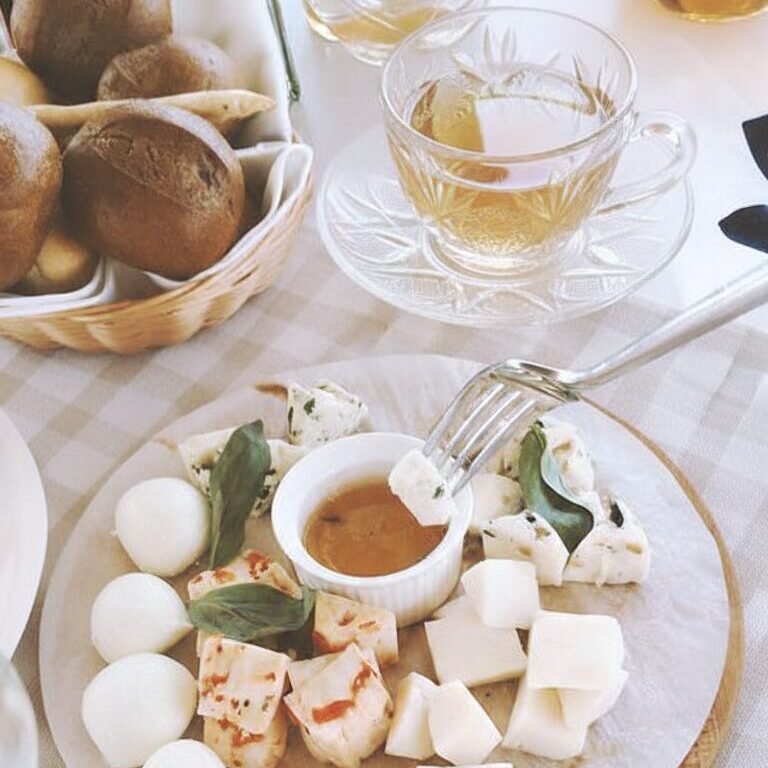 Cheese platter with assorted cheeses, bread, and tea on a cozy table setting. Perfect for a light brunch.