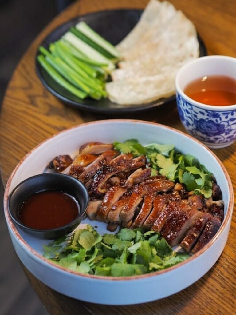Sliced roasted duck with cilantro, hoisin sauce, and tea on a wooden table. Asian food presentation.