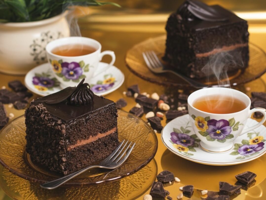 Chocolaty cake slices and steaming tea in floral cups on a golden table setting with scattered chocolate pieces.