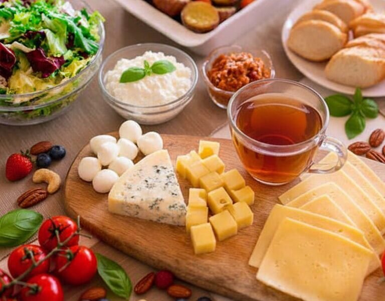 Cheese and salad brunch with tea, fresh fruits, and bread on a table setting, offering a variety of healthy options.