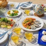 Elegant outdoor dining with seafood, salads, cheese, tea, and a strawberry cake on a beautifully set table.