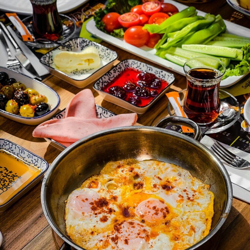 Turkish breakfast spread with fried eggs, fresh vegetables, olives, cheese, and tea on a wooden table.