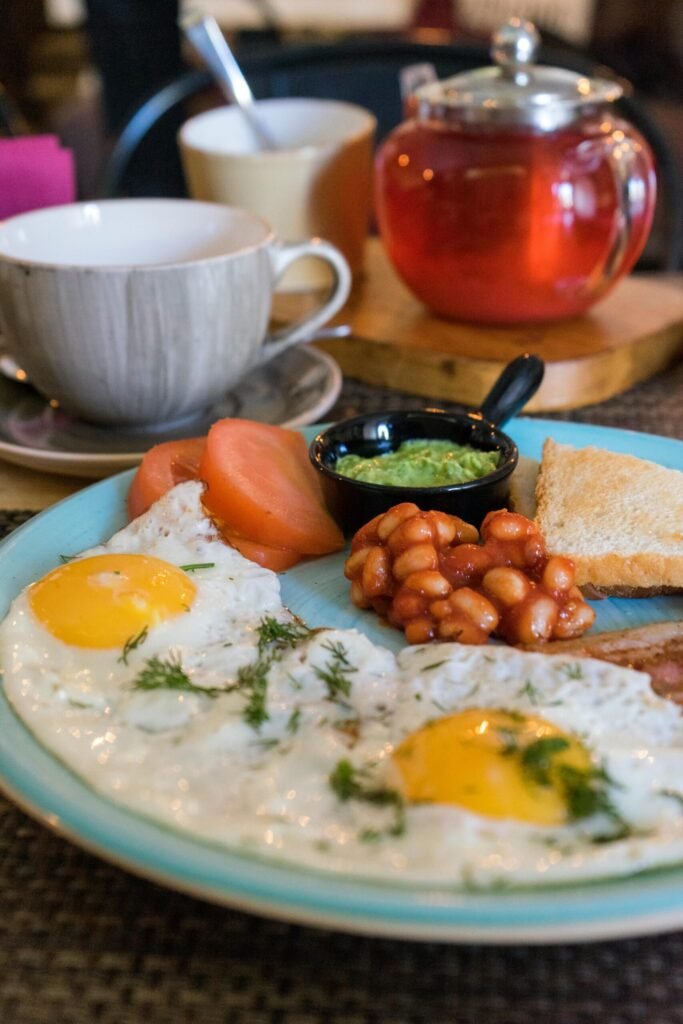 Breakfast plate with sunny-side-up eggs, beans, toast, tomatoes, green sauce, and tea. Perfect morning meal.