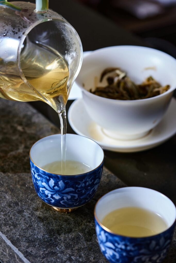 Pouring tea into a blue floral cup with a white bowl of tea leaves in the background.
