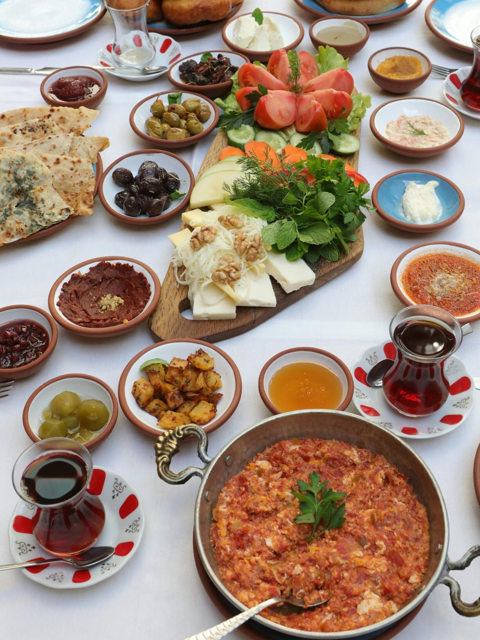 Traditional Turkish breakfast spread with tea, olives, cheeses, vegetables, and savory dishes on a table.