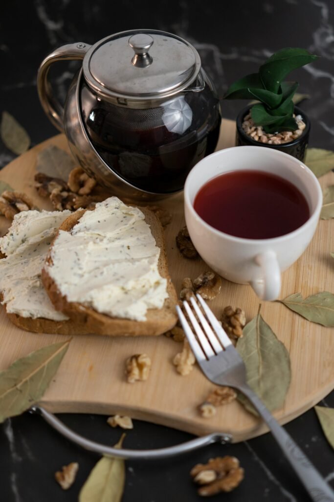 Breakfast setting with tea, toast with cream cheese, walnuts, and bay leaves on a wooden board.