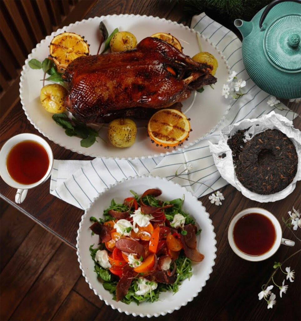 Roast duck with citrus, fresh salad, and tea served elegantly on a wooden table for a delicious meal.