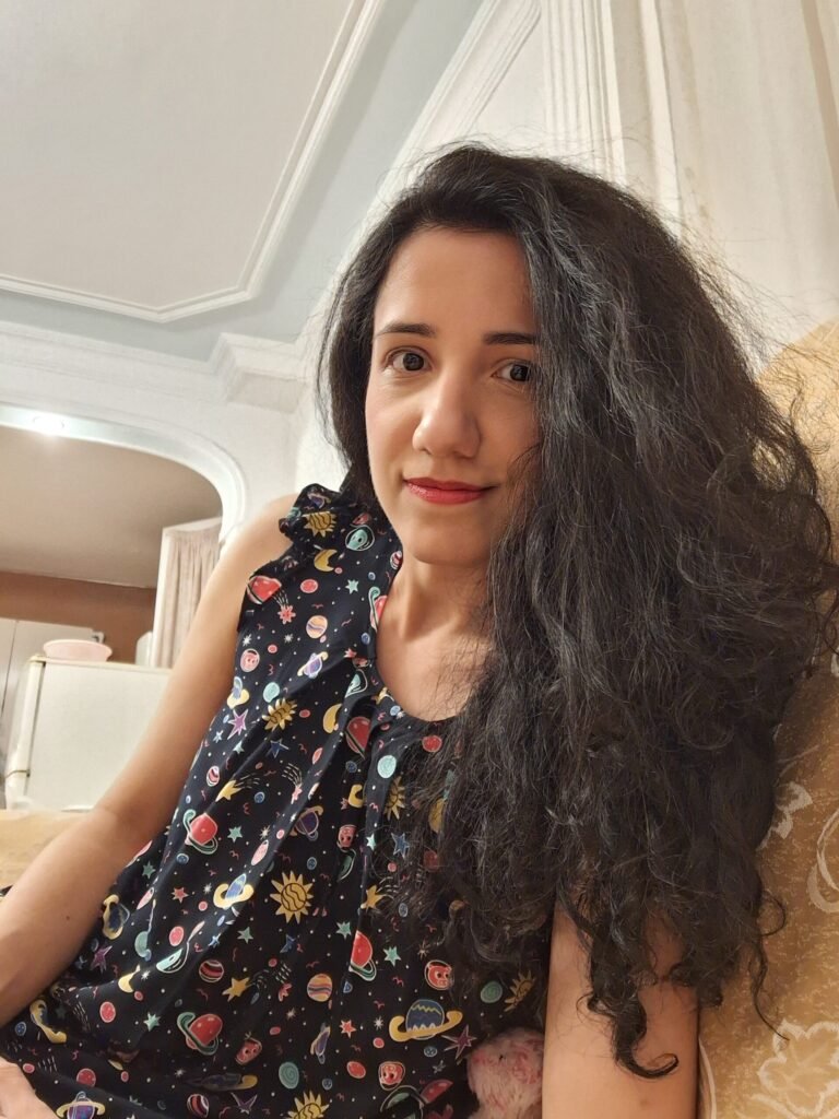 Woman in space-themed top sitting indoors with a relaxed expression.